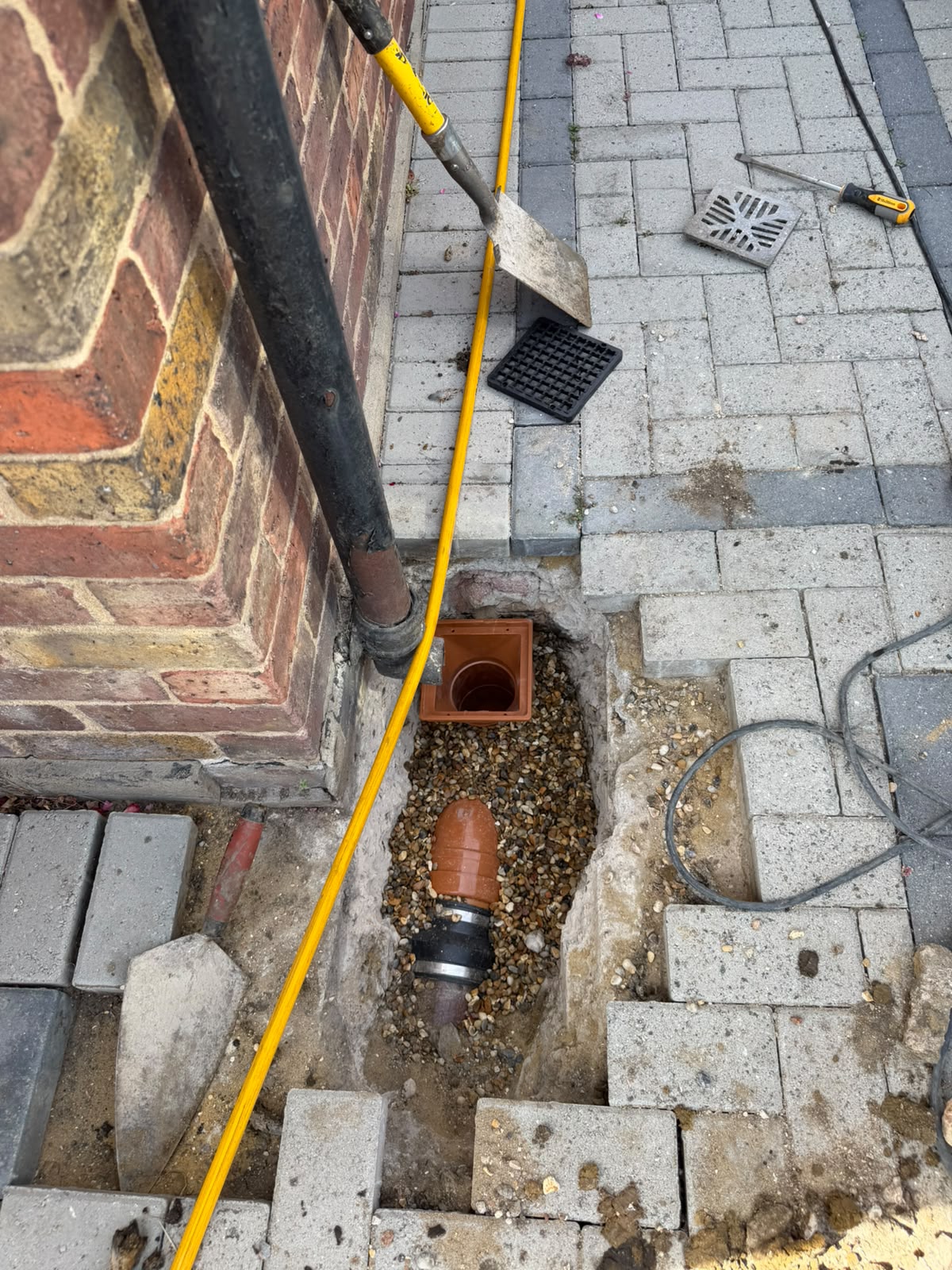 Excavated driveway with new gully pot and pipe connection being fitted