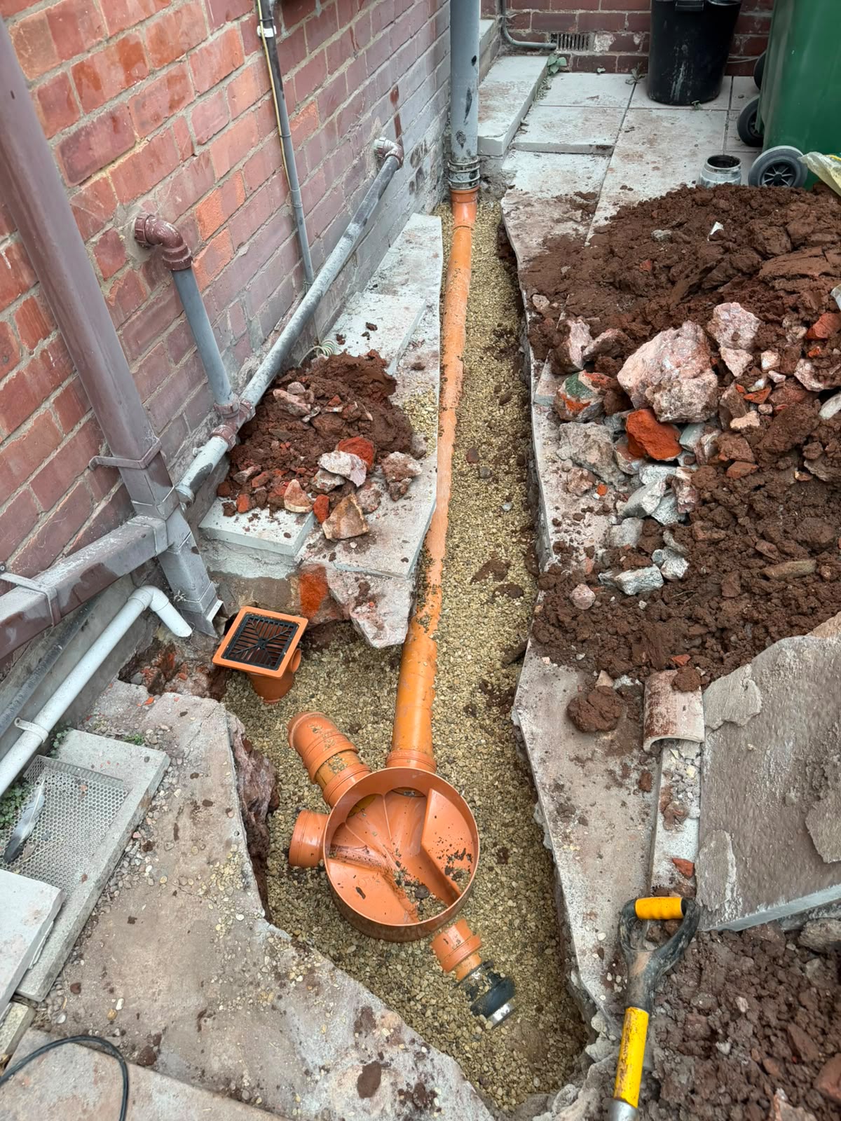 Rear yard excavated with new orange pipework and inspection chamber base in the trench