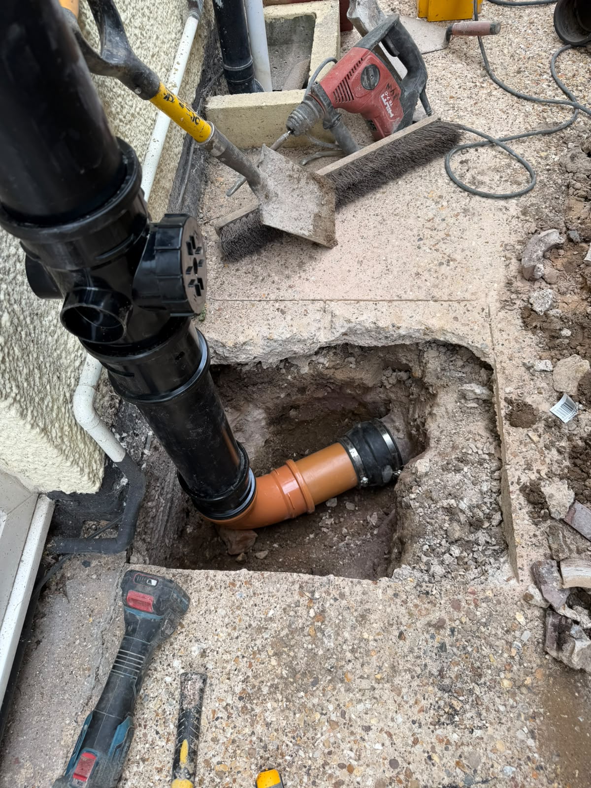 Concrete path broken out beside a house showing the old soil pipe bend